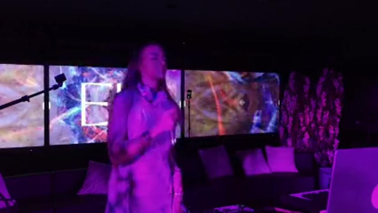 EIR stepping out from the decks, hand on heart, in flowing fabric under purple light